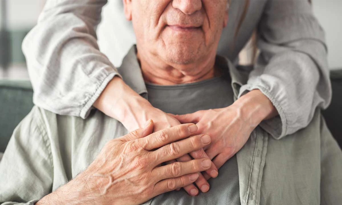 Close-up of an older man sitting with a caregiver’s arms gently wrapped around him, symbolizing support and connection in dementia and Alzheimer’s care.