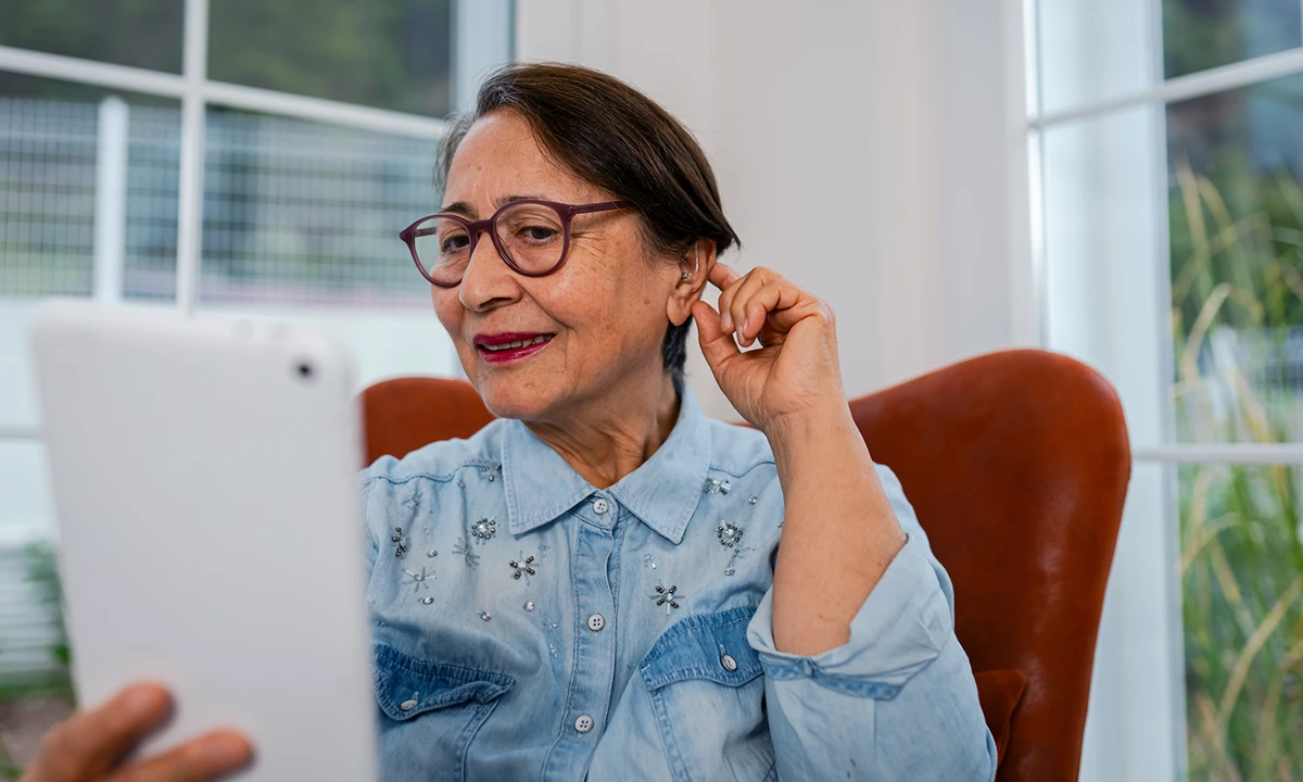 Senior holding a hand to their ear next to a list of common signs of hearing loss in older adults.