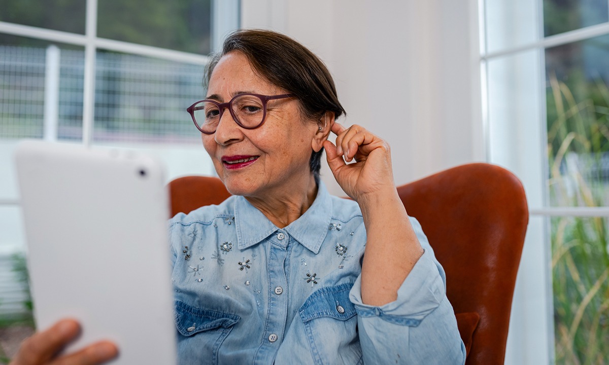 Senior holding a hand to their ear next to a list of common signs of hearing loss in older adults.