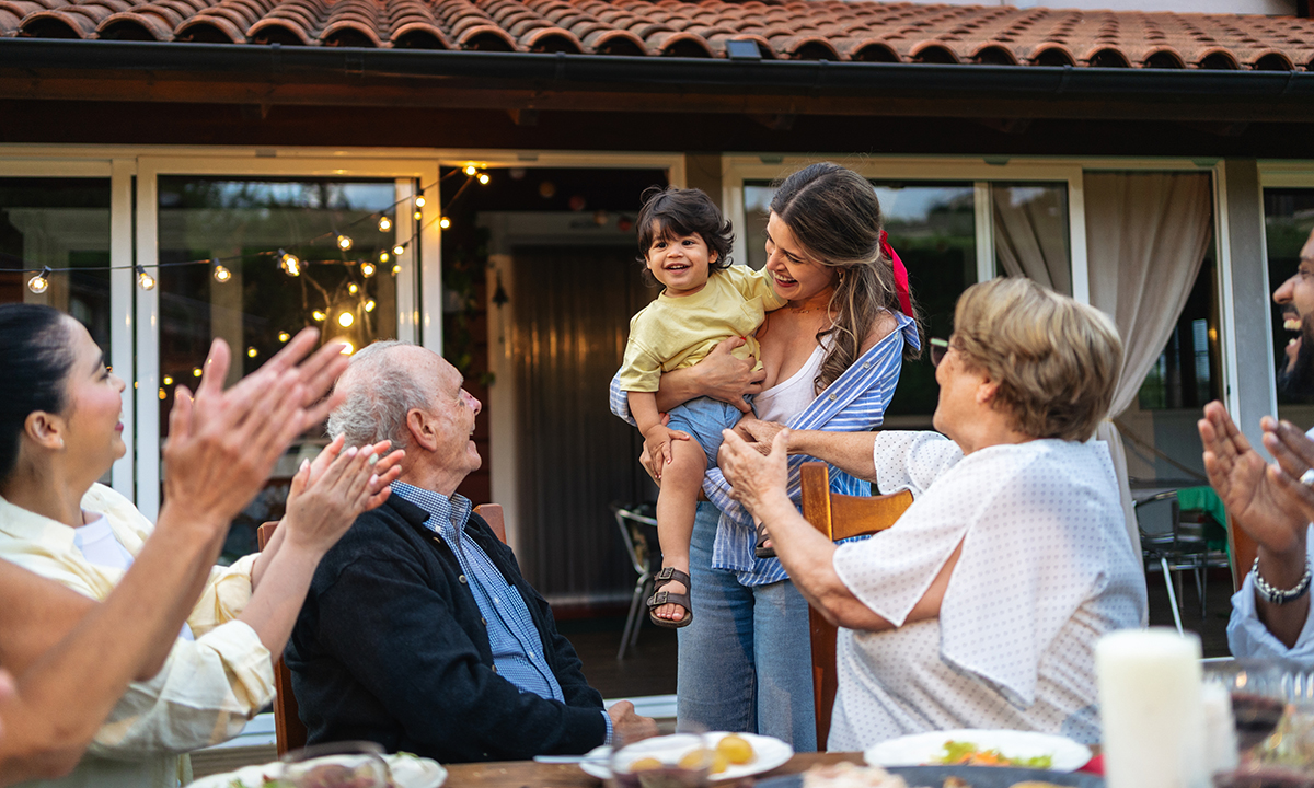 Large multi-generational family gathering, rejoicing newborn arrival with cheerful conversations, hugging relatives, enjoying sunset garden ambiance