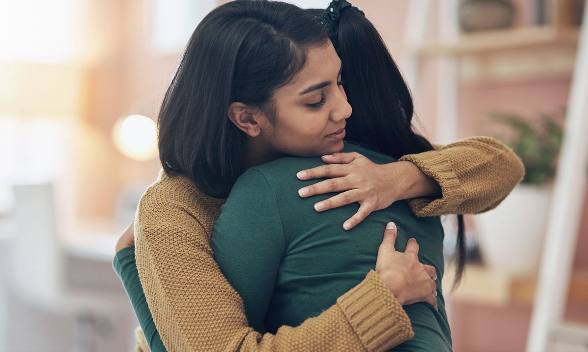 Two women embrace indoors, offering comfort and support during a moment of grief, conveying compassion, connection, and emotional care