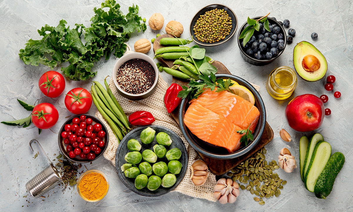 Overhead view of fresh, nutrient-rich foods including salmon, leafy greens, berries, avocado, legumes, tomatoes, and whole grains