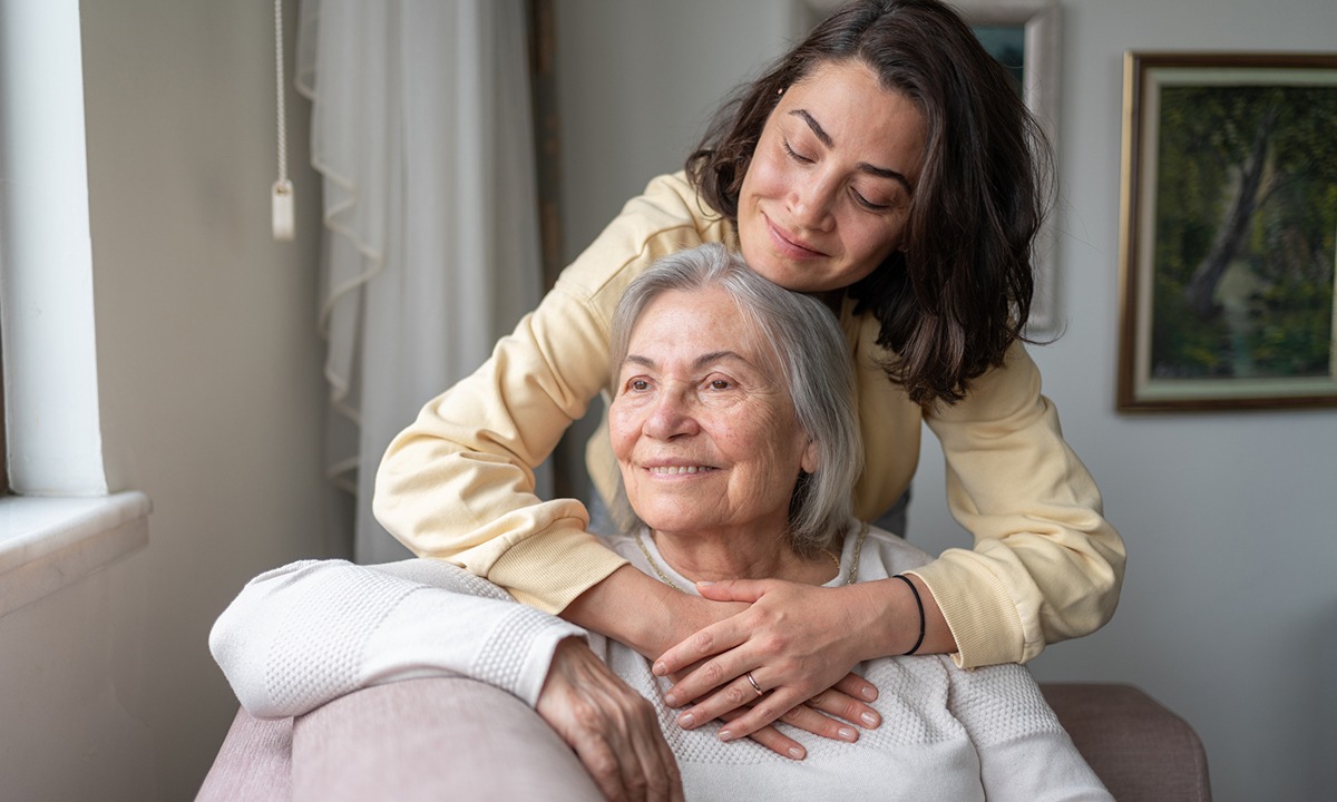 Older woman at home receiving support and companionship from a younger caregiver in a comfortable living space