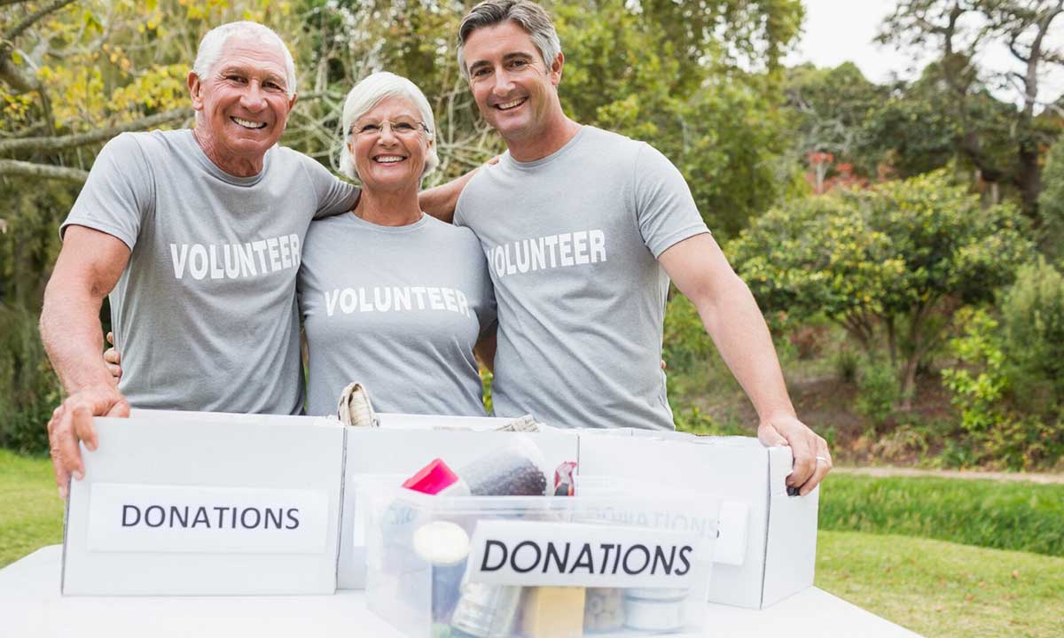 Three volunteers smiling while holding donation boxes outdoors.