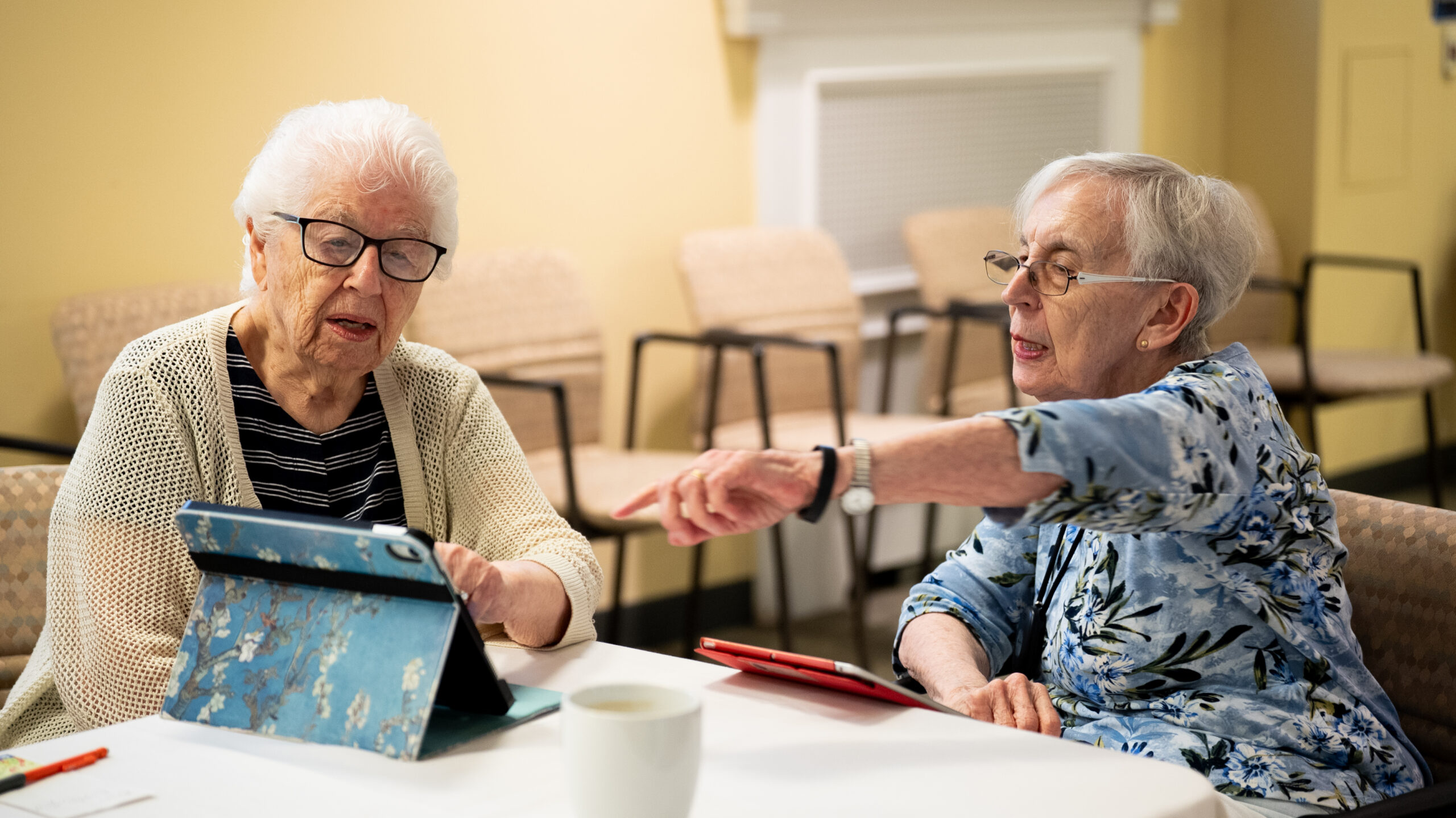 Still Learning – and Helping Others Do the Same Two Osborn residents seated at a table with tablets during the community's resident-run iPad Clinic